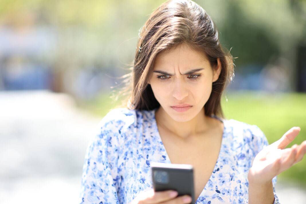Persona sosteniendo un teléfono móvil con un símbolo de escudo de seguridad en la pantalla, representando la limpieza de virus.