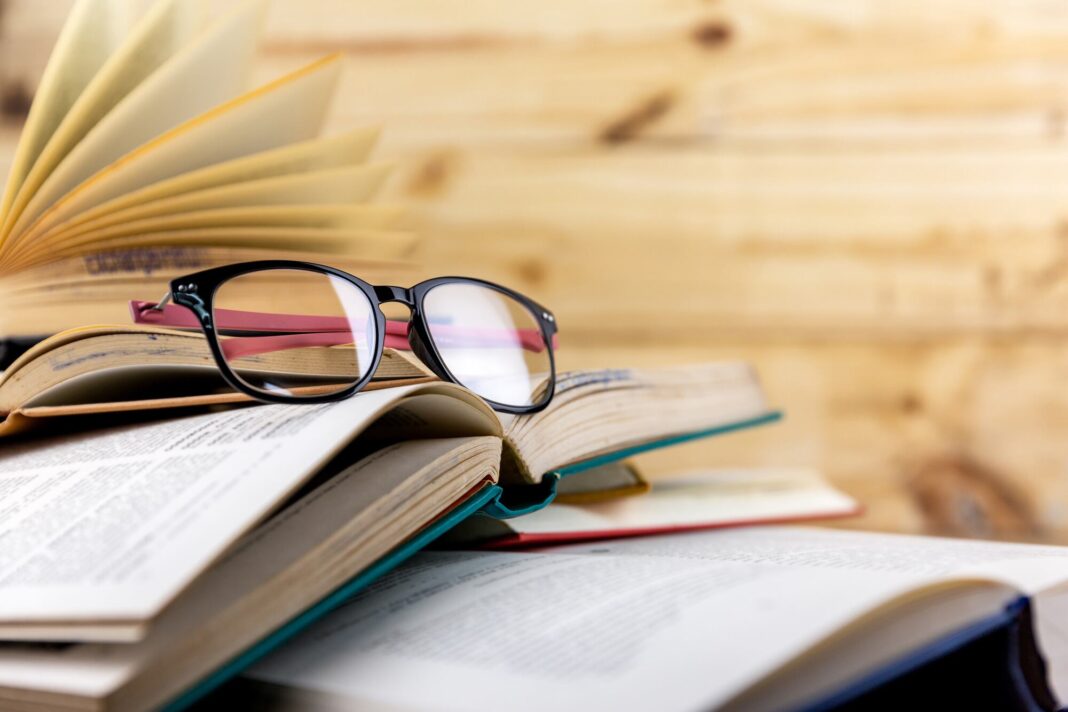 Montaje de varios libros clásicos apilados con una vela encendida sobre ellos, en alusión al Día del Libro