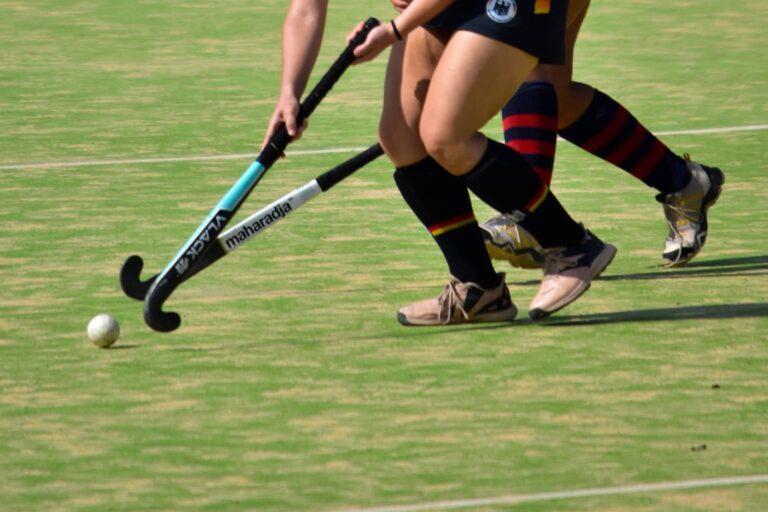 Ilustración de un campo de hockey con siluetas de jugadoras en el fondo.